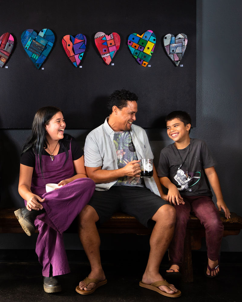 A happy family sits on a bench at a fun Maui café with bright colored hearts on the wall.