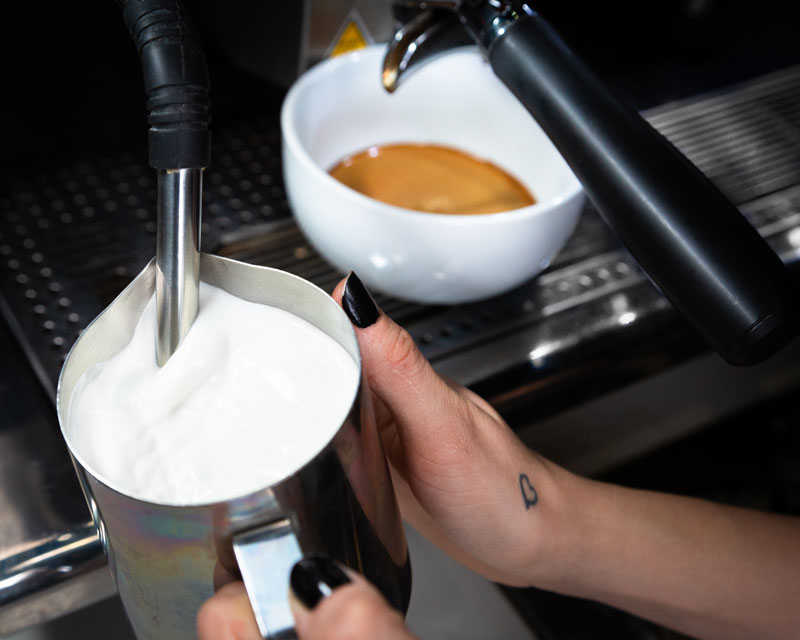 A Wailuku Coffee Company barista steaming milk into a metal cup in order to make a cafe latte.