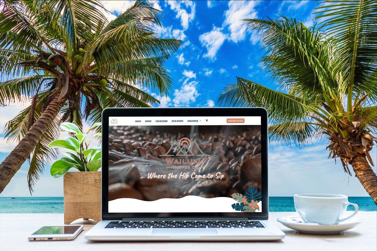 A laptop on a table with Coffee Buzz articles web page and palm trees and the ocean in Maui.