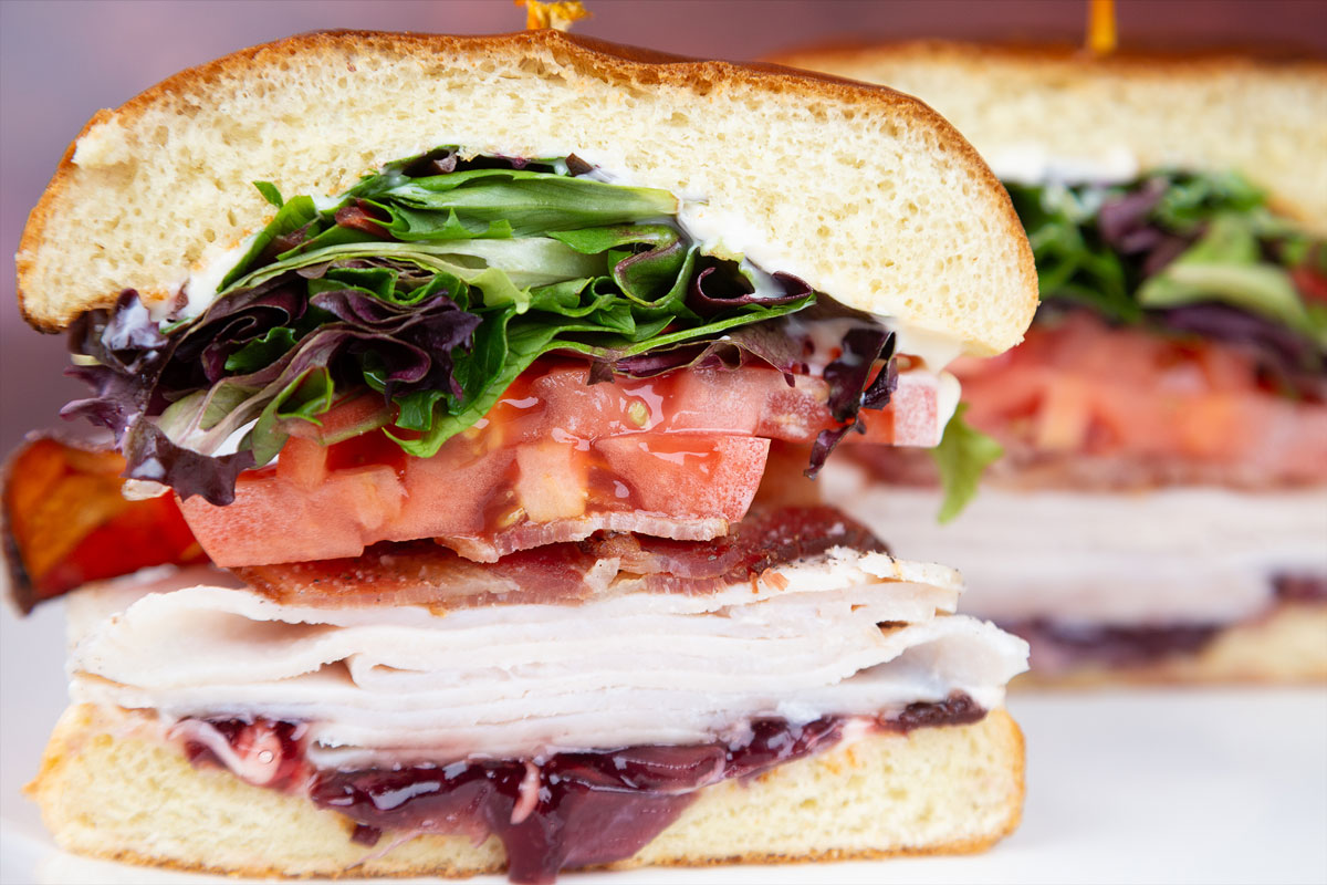 Juicy close-up view of a turkey, bacon, tomato, clubhouse sandwich on a white plate.