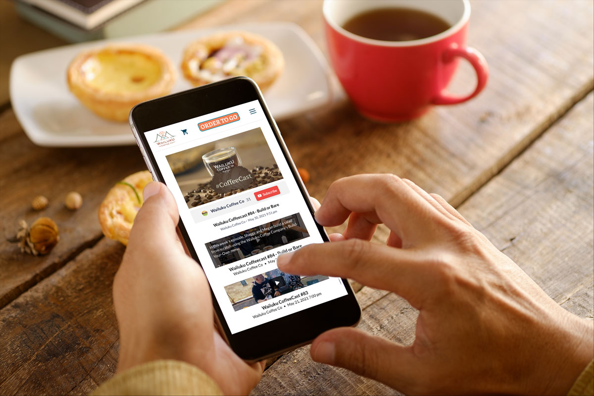 A person holding a phone while enjoying a cup of coffee and watching CoffeeCast.