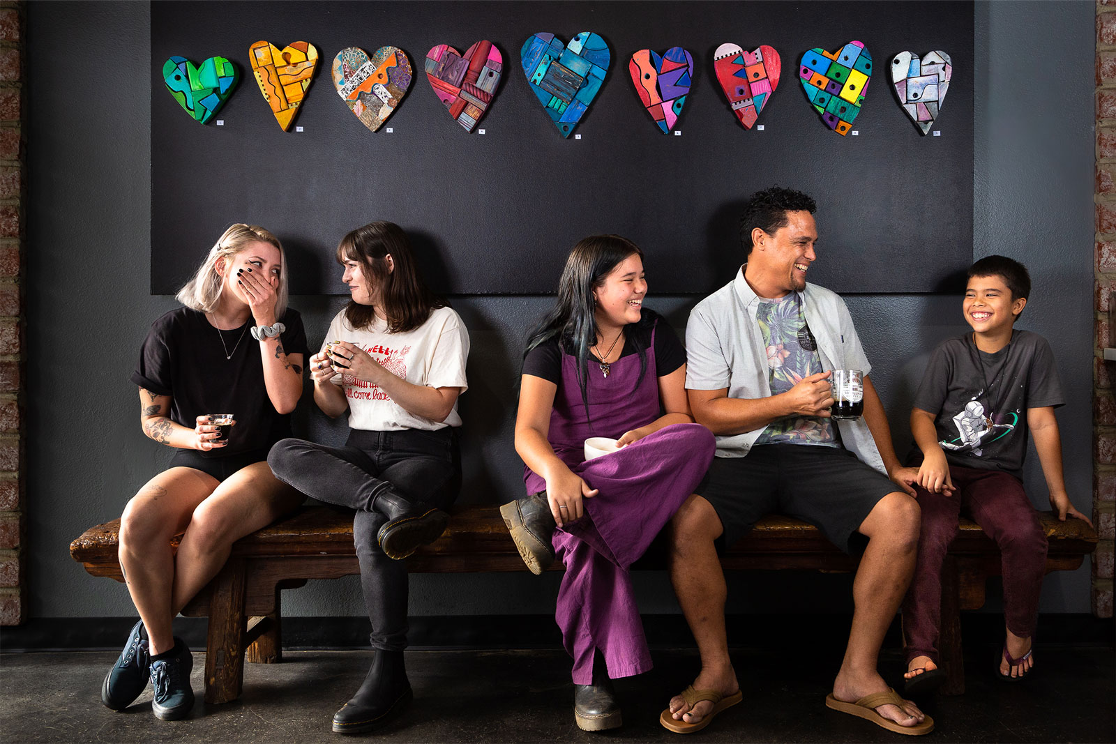 A group of people gather on a bench with hearts painted on the wall.