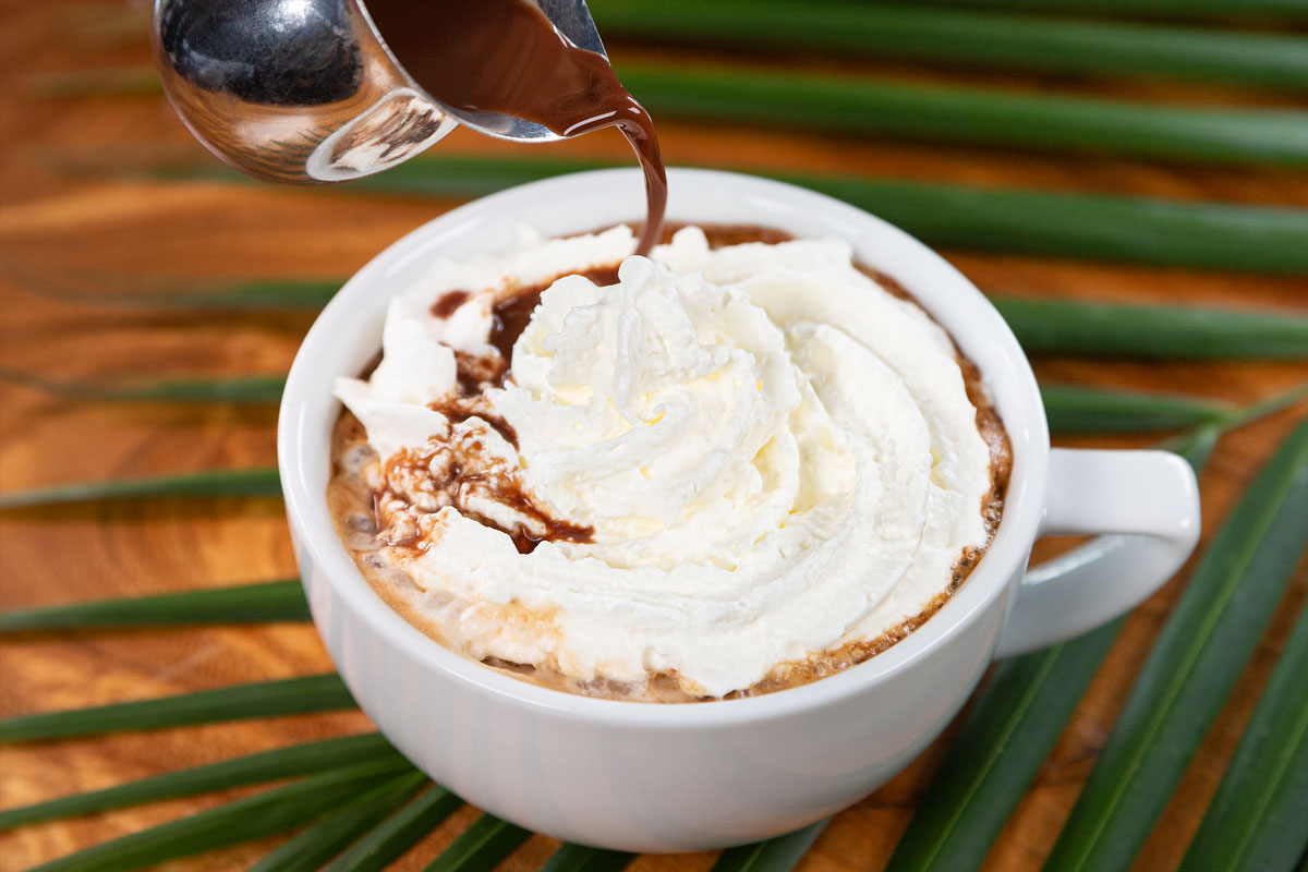 A cup of hot mocha latte with whipped cream and chocolate syrup poured on at a café in Maui.