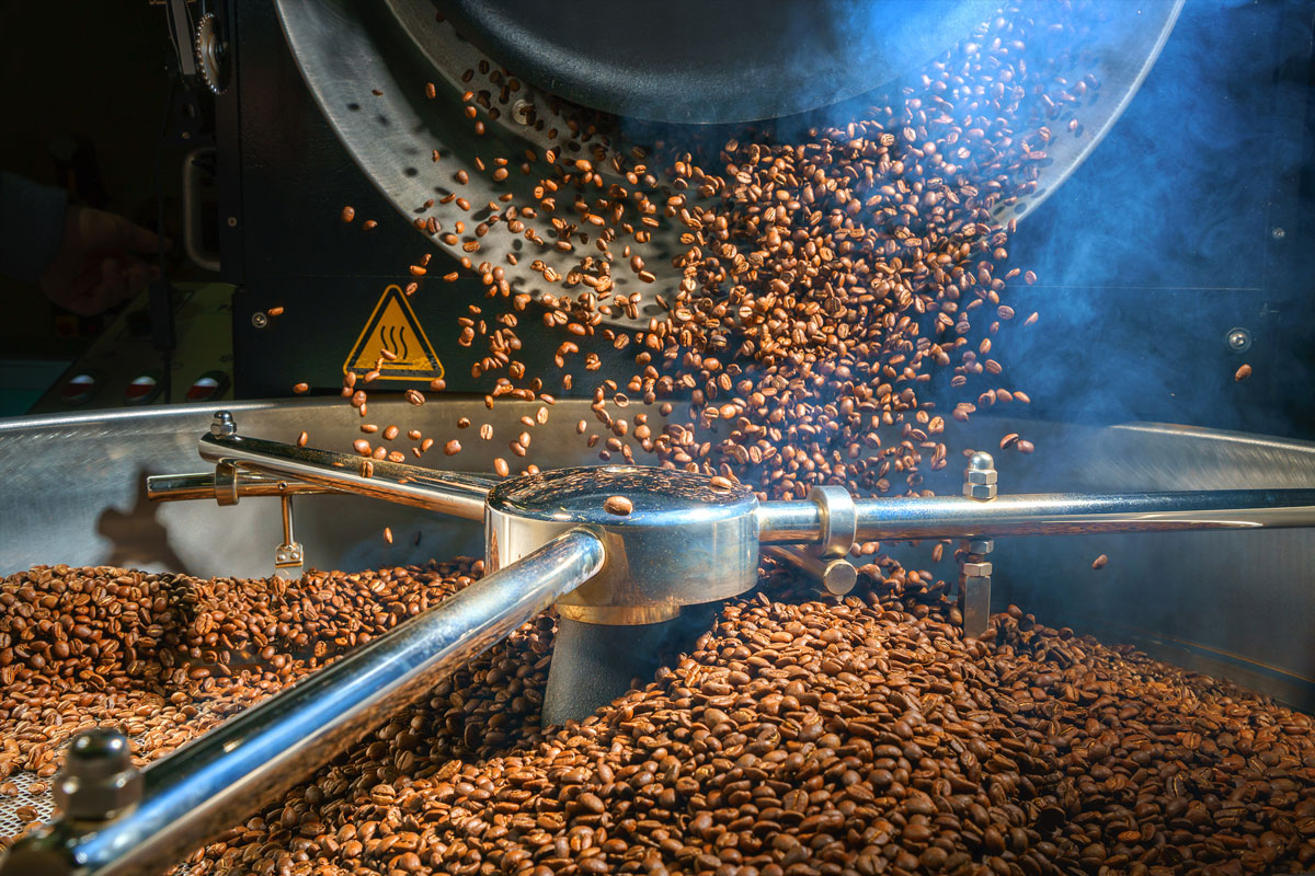 Roasting machine with coffee beans being poured into it.