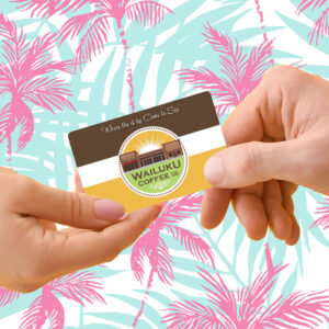 Two hands holding a Wailuku Coffee Co. cafe gift card for in-store purchases with a tropical palm pink and blue background.