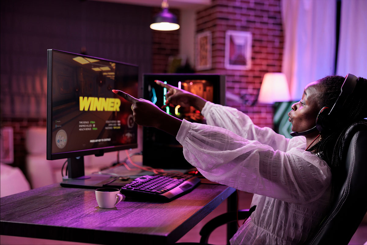 A person gaming, enjoying a cup of coffee, and pointing at a computer screen.